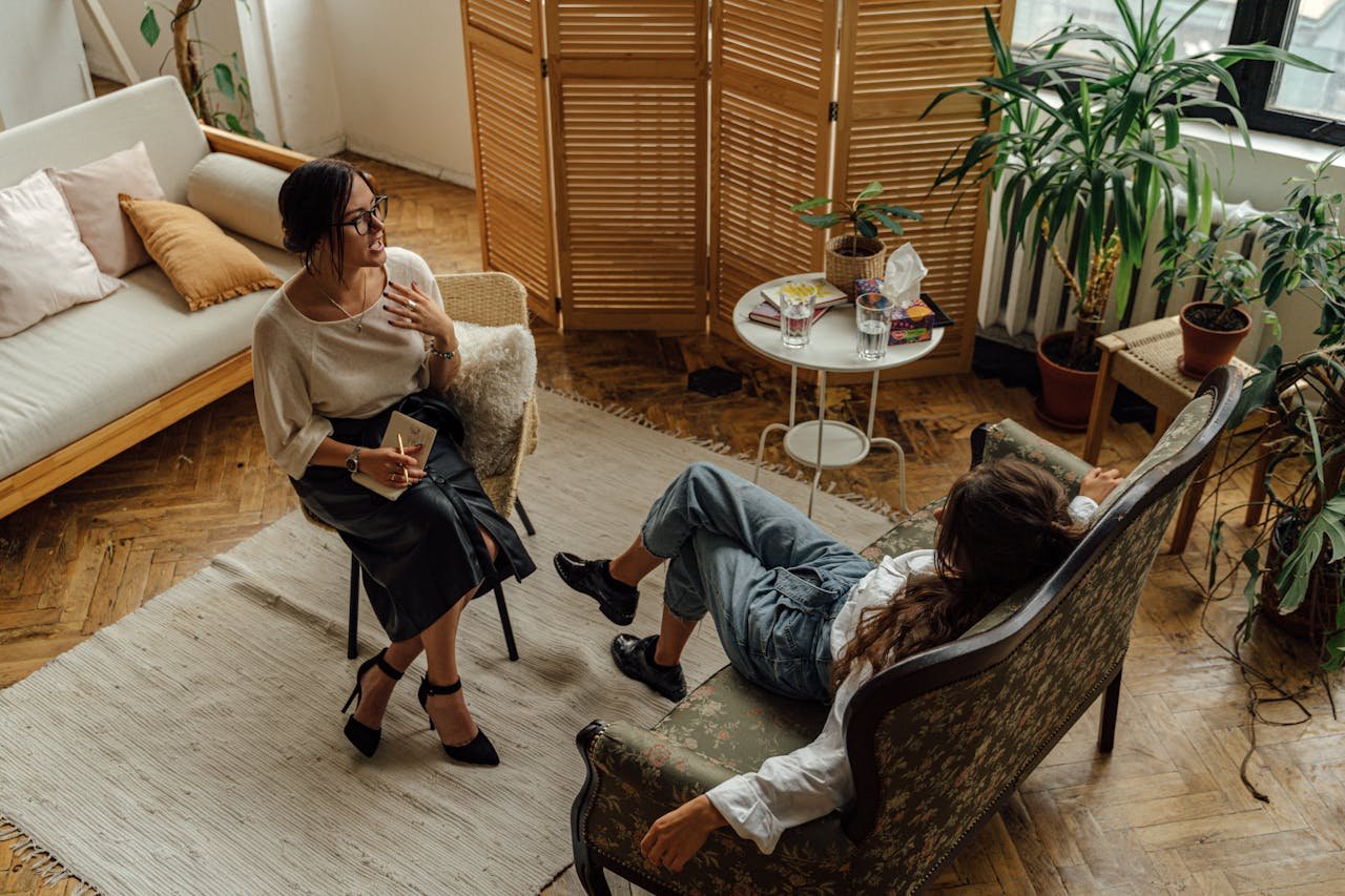 digital Two women engaged in a psychotherapy session in a warm, inviting interior with plants and natural lighting.